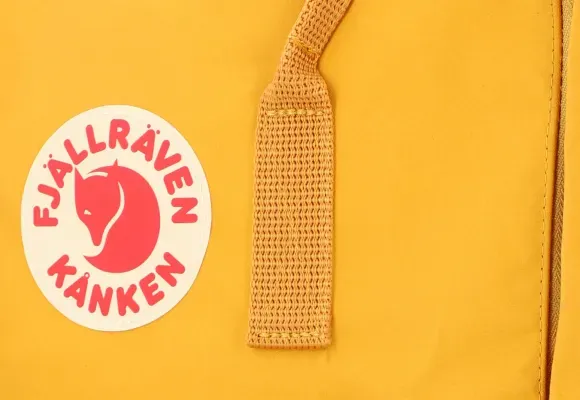 Nærbillede af logo og rem på gul Kanken-rygsæk